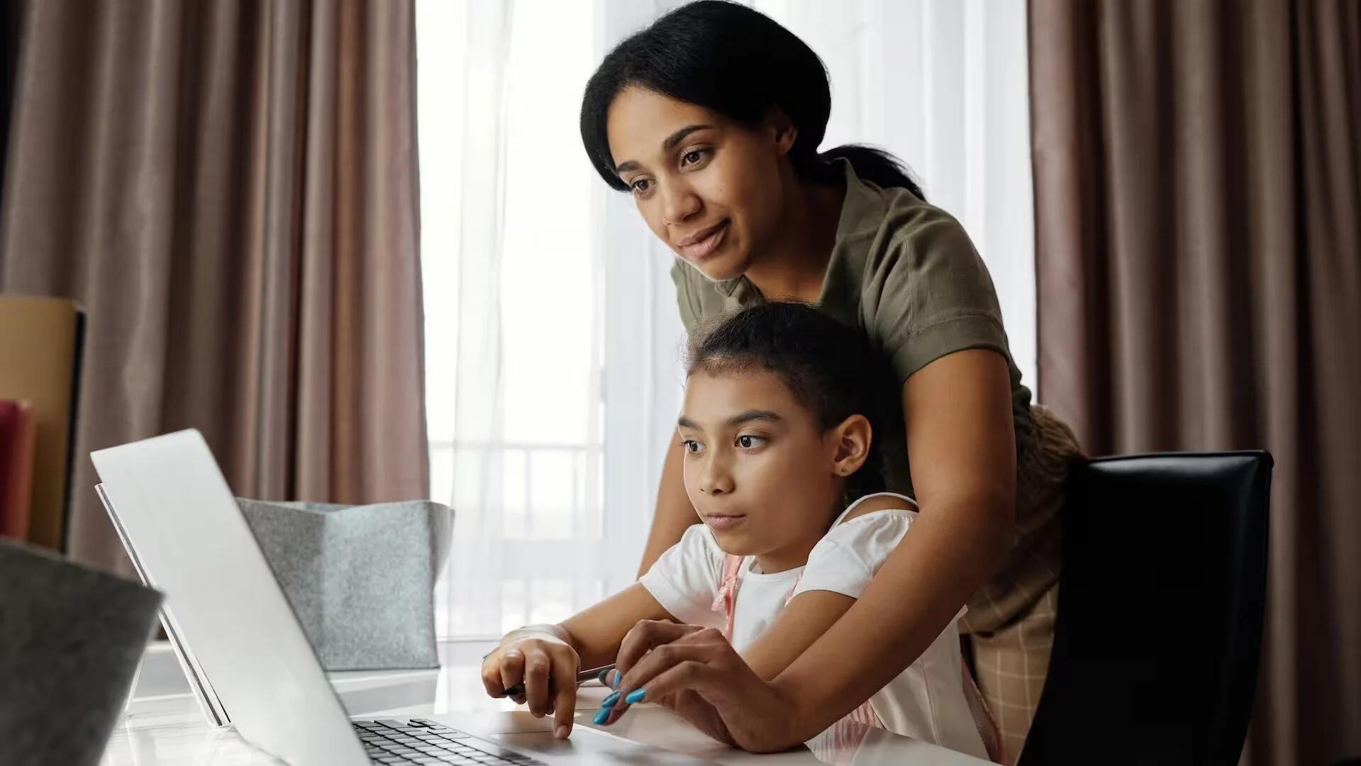 Mother Helping Her Daughter Use A Laptop